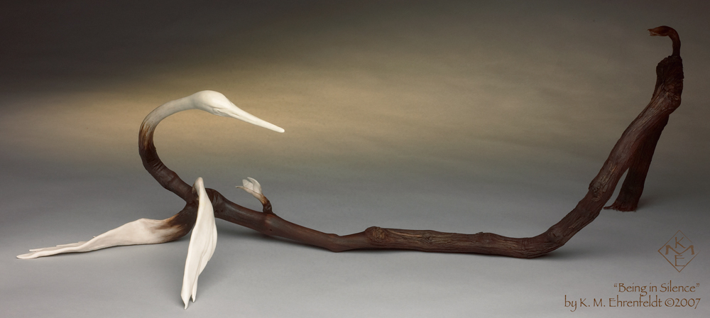 A ivory-hued porcelain egret head looks back over its sinewy form. One porcelain wing stretches flat along the surface below, holding its vine body up in this partial recline. The other wing reaches forward, tip touching surface to keep in balance. A few inches down the vine, leafy porcelain tail feathers erupt outward from the opposite side. The egret's body consists of a grapevine, gnarled and knotty, with smooth deep reddish brown wood, about one quarter the length of the whole grapevine stick. It seems to be emerging from the stick itself. Beyond that smooth point is the original fibrous bark covering the vine as it snakes along the surface then forms an upward arch about ten inches high, continuing back downward settling on the flat surface behind. At the top of the arch is a woodsy brown porcelain growth, protruding upward as an arched leaf or perhaps a new unformed egret head emerging.