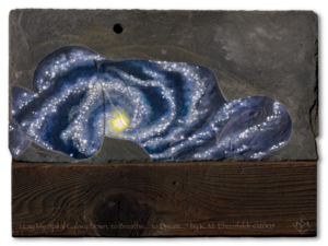A woman laying on her side etched into weathered slate is painted as a spiral galaxy. The slate rests atop a recycled barn wood post. The knot in the wood at the base lines up with the center light on the woman and the black velvet void of potential above.