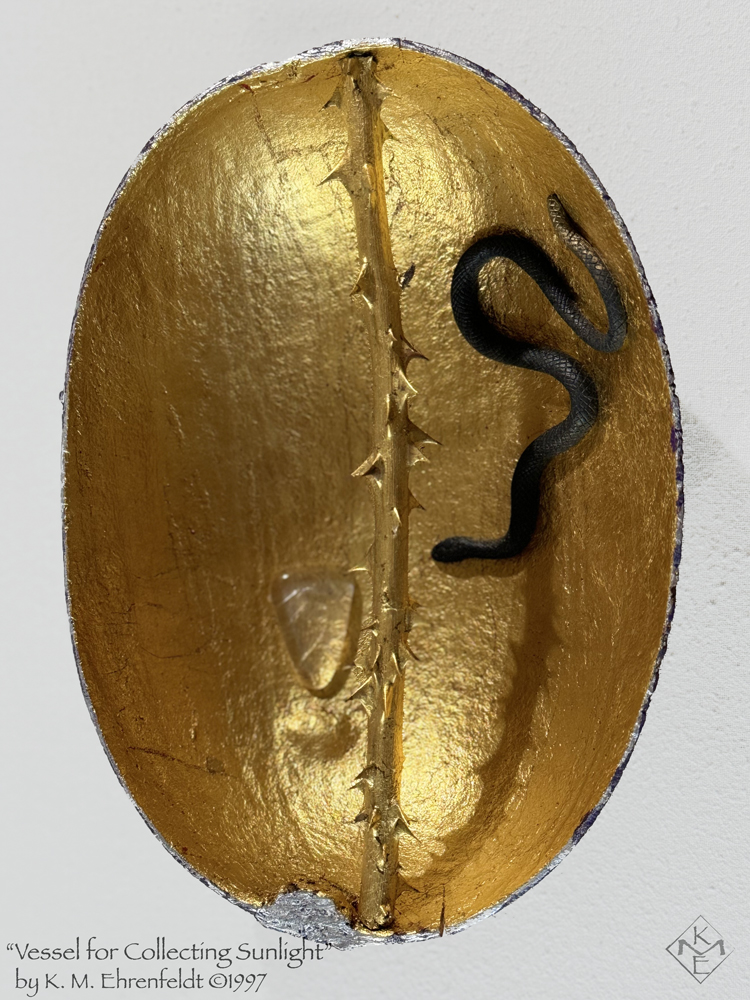 The Sun Vessel in full view reveals its gold-leafed interior with a thorny gold-leafed rose stem bisecting the gourd lengthwise across the top from stem to base, casting a shadow across. A black snake with golden tail curves across the bottom toward the center. On the opposite side of the thorny rod above, a clear glass triangle rests inside, pointing downward, and resembles a puddle of light. There is a crescent moon shaped shadow near the point of the triangle. The rim of the vessel is a deep blue and silver.