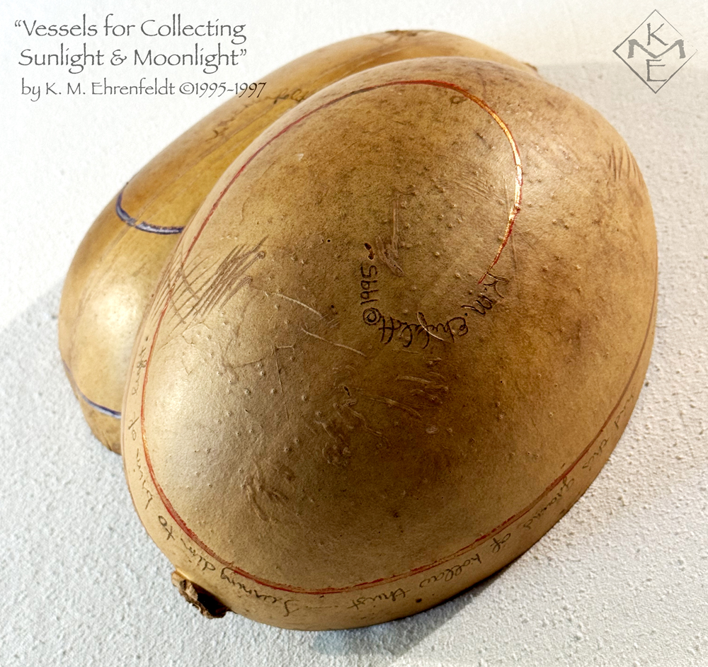 Showing a partial external side of the Sun Vessel, the Moon Vessel rests on top, also upside down. The raw amber surfaces of the gourds show the spiraling lines, red-gold on the Moon Vessel, and blue-silver on the Sun Vessel, moving from stems around to the center bottoms where the artist's signature is. Words visible on the Moon Vessel are underscored by a red-gold line.